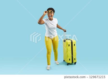 African american woman with big yellow suitcase isolated on blue wall. 129671215