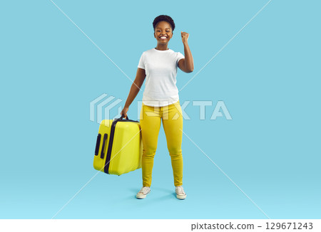 Happy woman carry on huge yellow suitcase on blue background. Lady with smile and victory gesture. Happy woman carry on huge yellow suitcase on blue background. Lady with smile and victory gesture. 129671243