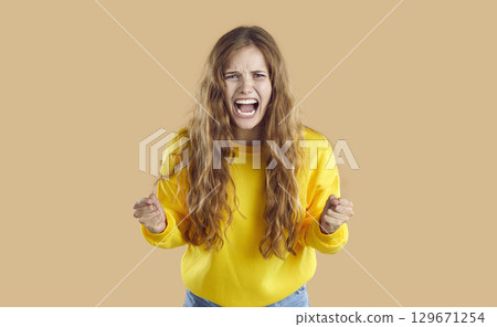 Frustrated emotional angry sad screaming young woman with clenched fists on beige background. Frustrated emotional angry sad screaming young woman with clenched fists on beige background. 129671254