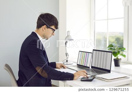 Man office worker is working with spreadsheets on computers screens and making calculations. Man office worker is working with spreadsheets on computers screens and making calculations. 129671255
