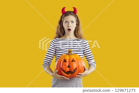 Beautiful young woman with funny surprised face expression holding Halloween pumpkin 129671275