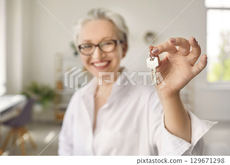 Happy senior middle aged woman customer landlord holding key to new house apartment. 129671298