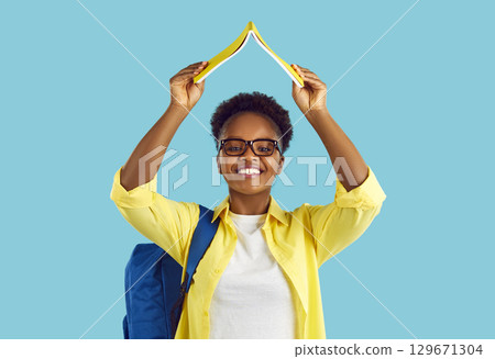 Portrait of happy school, college or university student girl holding book above her head 129671304