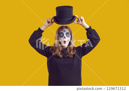 Little girl in Halloween costume putting on hat with funny surprised face expression 129671312