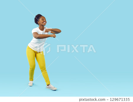 Happy funny African American woman in casual clothes dancing on blue copy space background 129671335
