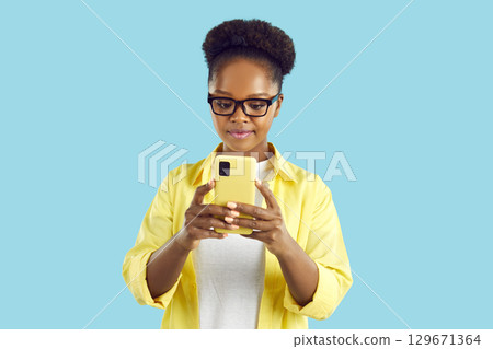 Serious woman in glasses using smartphone on turquoise background looking at screen. Serious woman in glasses using smartphone on turquoise background looking at screen. 129671364