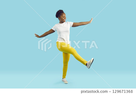 Cheerful funny woman joyfully walking with arms outstretched on vivid light blue background. 129671368