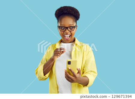 Happy excited amazed african american woman looking at smartphone screen on turquoise background. 129671394