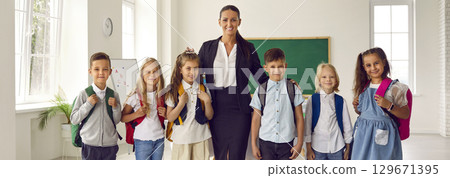Happy school teacher and first grade students in class. 129671395