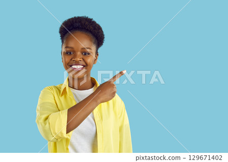 Portrait of attractive cheerful African American woman demonstrating copy empty space for ad advert. 129671402