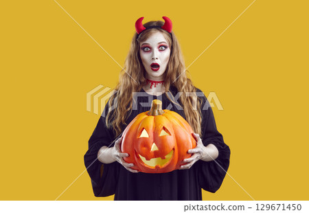 Surprised teen girl with Halloween makeup holding jack-o-lantern 129671450