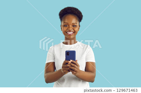 Happy smiling afroamerican woman with smartphone is looking at camera on turquoise background. 129671463