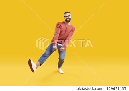 Full length portrait of funny bearded man in red sweatshirt and jeans dancing on yellow background. 129671465