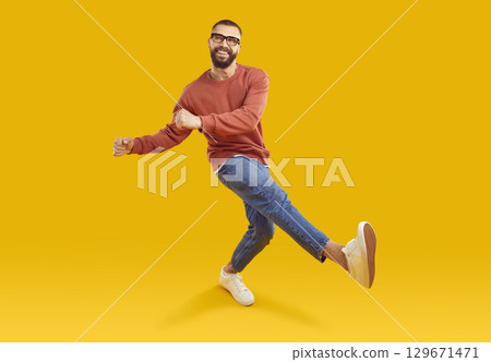Cheerful man in sweatshirt, jeans and glasses dancing isolated on yellow background Cheerful man in sweatshirt, jeans and glasses dancing isolated on yellow background 129671471