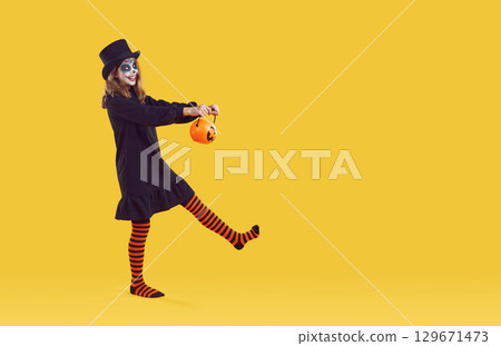 Happy child with Halloween trick or treat basket walking on yellow copy space studio background Happy child with Halloween trick or treat basket walking on yellow copy space studio background 129671473