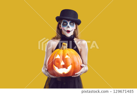 Funny surprised child in Halloween costume holding jack o lantern and looking at camera 129671485