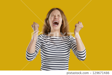 Funny young woman feeling very angry and frustrated, clenching fists and screaming Funny young woman feeling very angry and frustrated, clenching fists and screaming 129671486