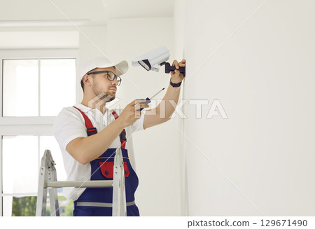 Male technician installs CCTV camera on wall in new bright office of business center. Male technician installs CCTV camera on wall in new bright office of business center. 129671490