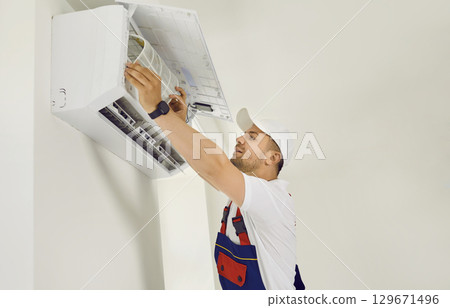 Male technician is cleaning and replacing air conditioner filter that hangs on wall inside house. 129671496