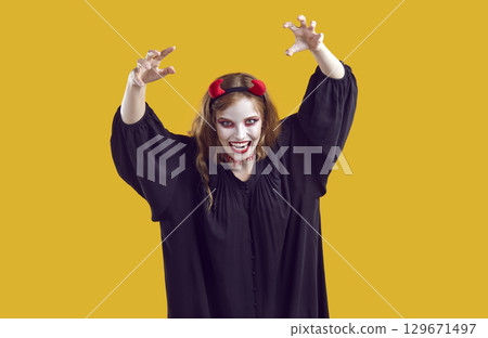 Young woman in spooky Halloween costume with devil horns isolated on yellow background 129671497
