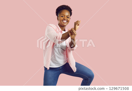 Cheerful dark-skinned woman is fooling around and having fun to moving and rhythmic music. Cheerful dark-skinned woman is fooling around and having fun to moving and rhythmic music. 129671508