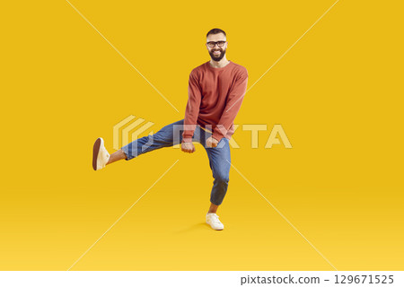 Smiling funky cheerful man in glasses dancing on one leg on yellow background. 129671525