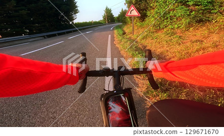 First person view of a cyclist riding along a mountain road at sunrise with a curve warning sign visible. Sport, training and healthy lifestyle concept First person view of a cyclist riding along a mountain road at sunrise with a curve warning sign visible. Sport, training and healthy lifestyle concept 129671670
