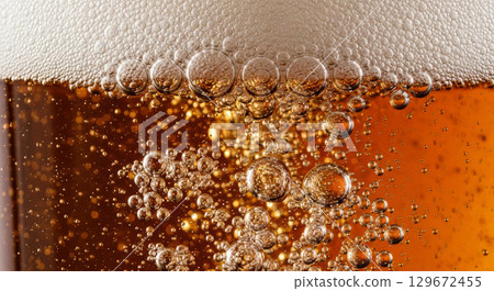 A macro shot captures the effervescent texture of a glass of beer, focusing on the rising bubbles and creamy foam.  129672455