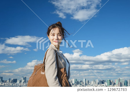 一位年輕女子在藍天和城市景觀的背景下微笑著站立的生活方式 一位年輕女子在藍天和城市景觀的背景下微笑著站立的生活方式 129672783