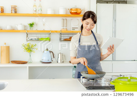 一位女士站在廚房裡，手裡拿著平板電腦 129673496