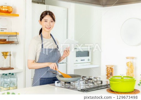 一位女士站在廚房裡，手裡拿著平板電腦 129673498