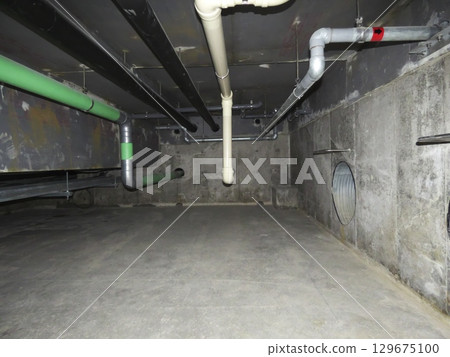 A complex network of pipes in an underground pit in a commercial building A complex network of pipes in an underground pit in a commercial building 129675100
