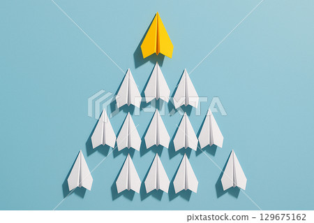A yellow paper airplane positioned at the top of a triangular group of white airplanes representing leadership hierarchy A yellow paper airplane positioned at the top of a triangular group of white airplanes representing leadership hierarchy 129675162