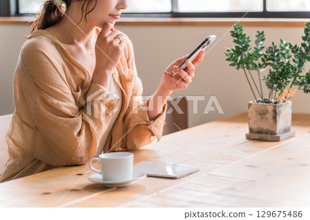 Young Asian woman looking at her smartphone while drinking coffee in a cafe (meeting) Young Asian woman looking at her smartphone while drinking coffee in a cafe (meeting) 129675486