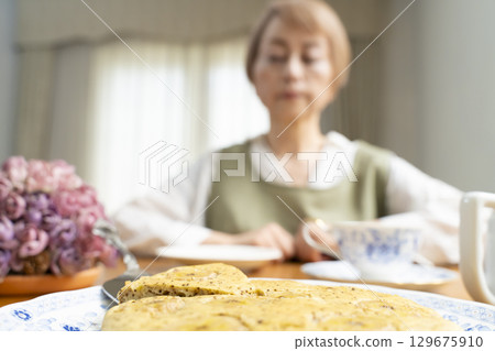 A senior woman baking a cake and making tea to enjoy her own time 129675910