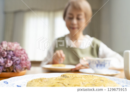 A senior woman baking a cake and making tea to enjoy her own time 129675915