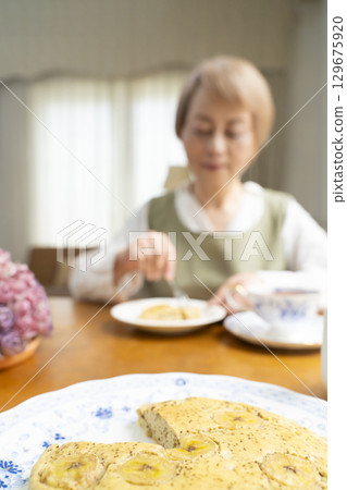 一位老婦人正在烤蛋糕、泡茶，享受自己的時光 129675920