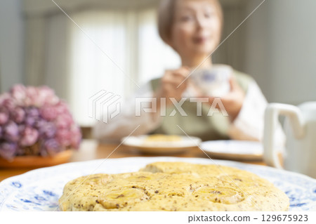 A senior woman baking a cake and making tea to enjoy her own time 129675923