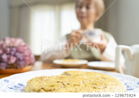 一位老婦人正在烤蛋糕、泡茶,享受自己的時光 一位老婦人正在烤蛋糕、泡茶,享受自己的時光 129675924
