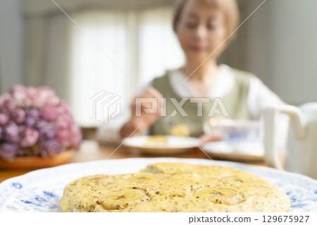 A senior woman baking a cake and making tea to enjoy her own time 129675927