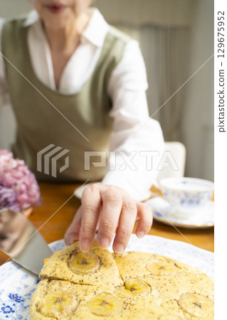 一位老婦人正在烤蛋糕、泡茶，享受自己的時光。臉上沒有表情。 129675952
