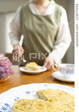 一位老婦人正在烤蛋糕、泡茶,享受自己的時光。臉上沒有表情。 一位老婦人正在烤蛋糕、泡茶,享受自己的時光。臉上沒有表情。 129675956