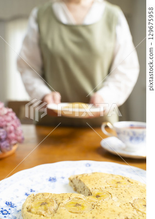 一位老婦人正在烤蛋糕、泡茶，享受自己的時光。臉上沒有表情。 129675958