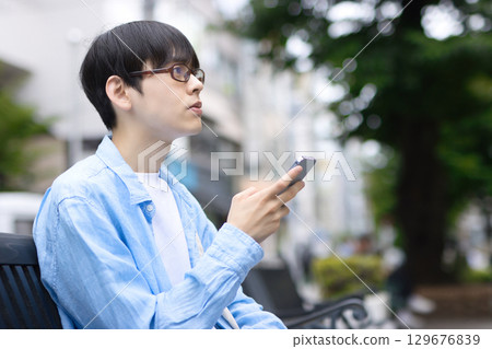 A young man sitting on a bench in the city and looking at his smartphone A young man sitting on a bench in the city and looking at his smartphone 129676839