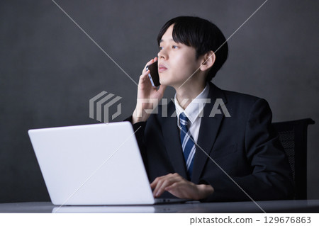 A young businessman talking on a smartphone while looking at a computer A young businessman talking on a smartphone while looking at a computer 129676863