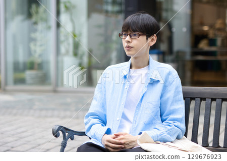 Young man sitting on a bench in the city Young man sitting on a bench in the city 129676923