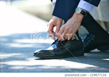 一位穿著西裝的年輕男子正在繫上商務鞋的鞋帶 129677116