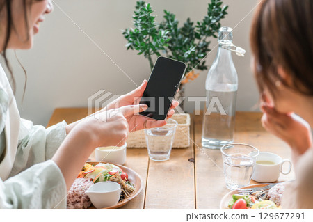 Cafe, coffee shop, woman's hands talking while looking at smartphone at dining table 129677291
