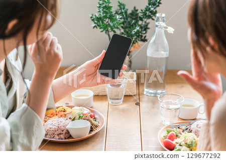 Cafe, coffee shop, woman's hands talking while looking at smartphone at dining table 129677292