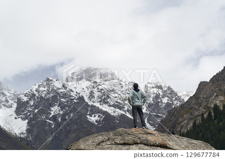 asian man standing on top of rock looking at peak of snow mountain asian man standing on top of rock looking at peak of snow mountain 129677784